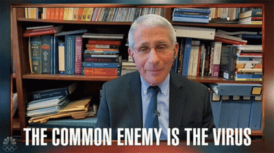 A Man In A Suit And Tie Stands In Front Of A Bookshelf With The Words " The Common Enemy Is The Virus " GIF