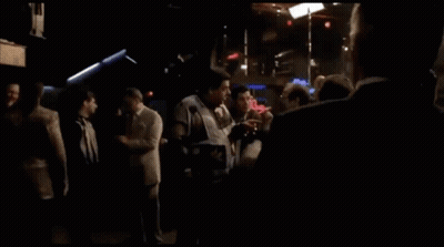 A Man In A Suit And Tie Stands In Front Of A Budweiser Sign GIF