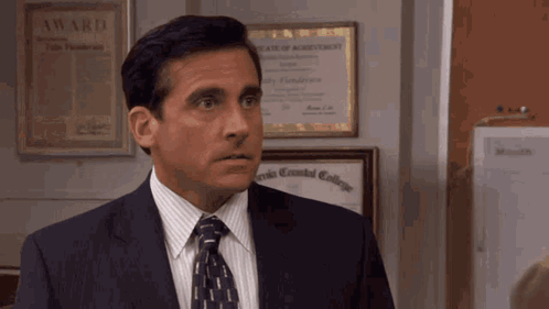 A Man In A Suit And Tie Stands In Front Of A Bulletin Board With A Certificate Of Agreement On It GIF