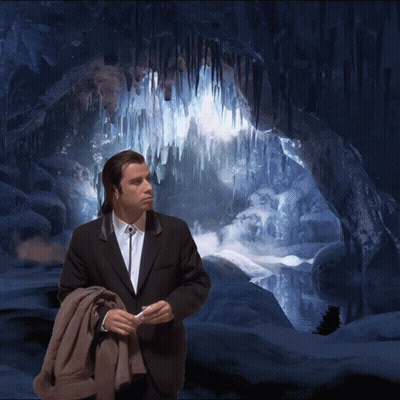 A Man In A Suit And Tie Stands In Front Of A Cave With Icicles Hanging From The Ceiling GIF