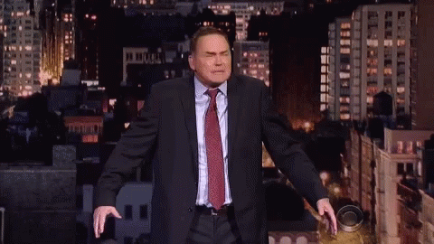A Man In A Suit And Tie Stands In Front Of A City Skyline At Night GIF