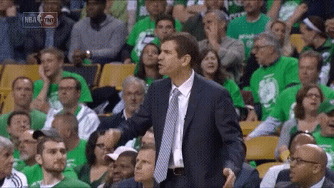 A Man In A Suit And Tie Stands In Front Of A Crowd At A Basketball Game GIF