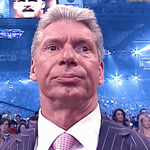 A Man In A Suit And Tie Stands In Front Of A Crowd At A Wrestling Match GIF
