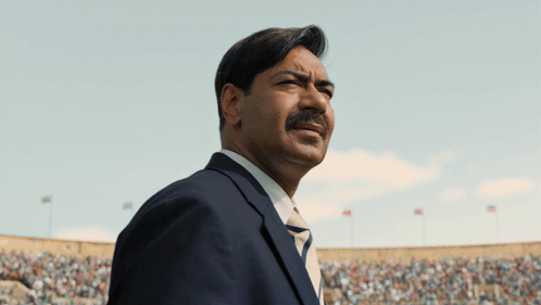 A Man In A Suit And Tie Stands In Front Of A Crowd In A Stadium GIF