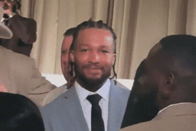 A Man In A Suit And Tie Stands In Front Of A Crowd GIF