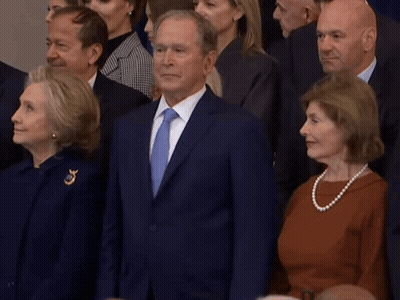 A Man In A Suit And Tie Stands In Front Of A Crowd Of People GIF