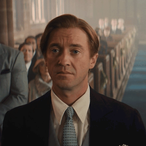 A Man In A Suit And Tie Stands In Front Of A Crowd Of People GIF