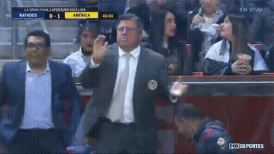 A Man In A Suit And Tie Stands In Front Of A Crowd Watching A Soccer Game Between Rayados And America GIF
