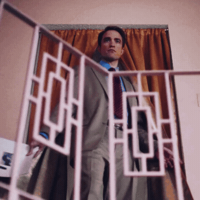 A Man In A Suit And Tie Stands In Front Of A Curtain GIF