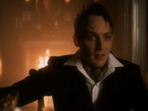 A Man In A Suit And Tie Stands In Front Of A Fire GIF