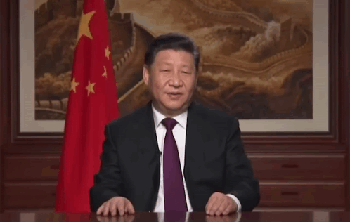 A Man In A Suit And Tie Stands In Front Of A Flag With The Words Wazzup Beijing Written On The Bottom GIF