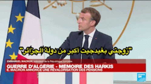 A Man In A Suit And Tie Stands In Front Of A Flag GIF