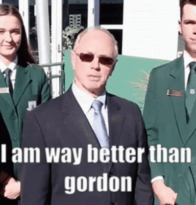 A Man In A Suit And Tie Stands In Front Of A Group Of People With The Caption I Am Way Better Than Gordon . GIF