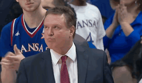 A Man In A Suit And Tie Stands In Front Of A Kansas Basketball Team GIF