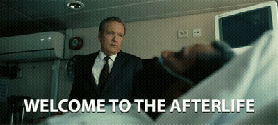 A Man In A Suit And Tie Stands In Front Of A Man In A Hospital Bed With The Words Welcome To The Afterlife Written Below GIF