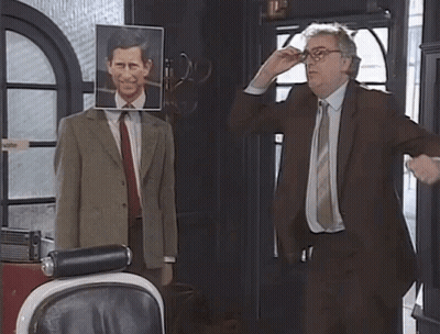 A Man In A Suit And Tie Stands In Front Of A Mannequin With A Picture Of Prince Charles On It GIF