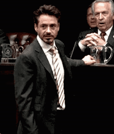 A Man In A Suit And Tie Stands In Front Of A Microphone GIF