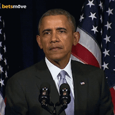A Man In A Suit And Tie Stands In Front Of A Microphone With A Betsmove Logo In The Background GIF