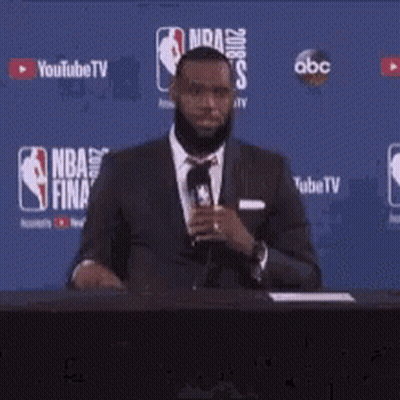 A Man In A Suit And Tie Stands In Front Of A Nba Finals Sign GIF