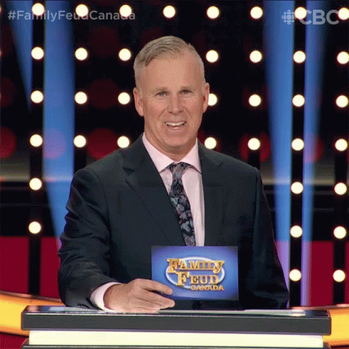 A Man In A Suit And Tie Stands In Front Of A Podium With A Sign That Says Family Feud Canada GIF