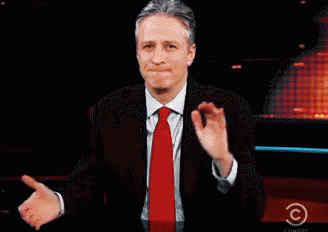 A Man In A Suit And Tie Stands In Front Of A Screen That Says Comedy Central GIF