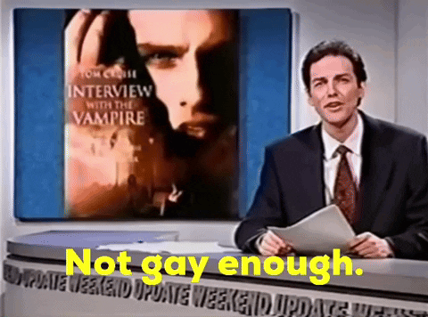 A Man In A Suit And Tie Stands In Front Of A Screen That Says Interview With The Vampire On It GIF