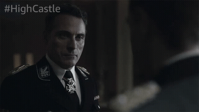 A Man In A Suit And Tie Stands In Front Of A Sign That Says #Highcastle On It GIF