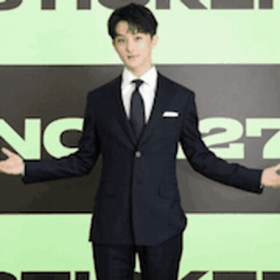 A Man In A Suit And Tie Stands In Front Of A Sign That Says Nc27 GIF