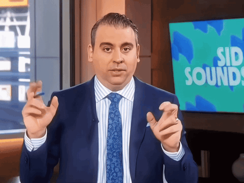 A Man In A Suit And Tie Stands In Front Of A Sign That Says Sid Sounds GIF