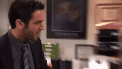 A Man In A Suit And Tie Stands In Front Of A Stack Of Papers GIF
