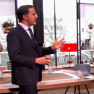 A Man In A Suit And Tie Stands In Front Of A Table With A Red Lamp On It GIF