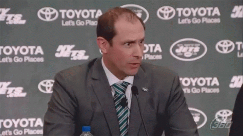 A Man In A Suit And Tie Stands In Front Of A Toyota Banner GIF