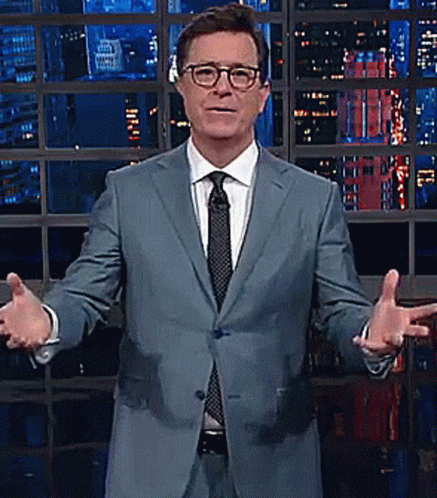 A Man In A Suit And Tie Stands In Front Of A Window GIF
