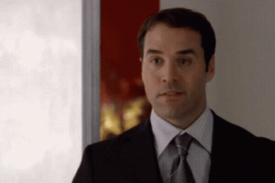 A Man In A Suit And Tie Stands In Front Of A Window GIF