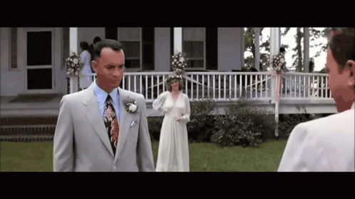 A Man In A Suit And Tie Stands In Front Of A Woman In A Wedding Dress GIF