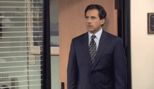 A Man In A Suit And Tie Stands In Front Of A Wooden Door GIF