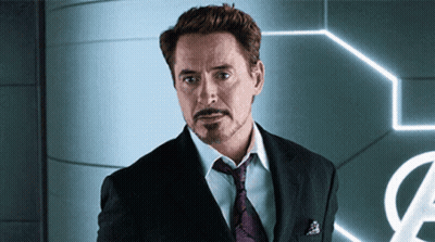 A Man In A Suit And Tie Stands In Front Of An Avengers Sign GIF