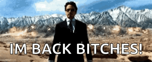 A Man In A Suit And Tie Stands In Front Of Mountains And Says I 'M Back Bitches ! GIF