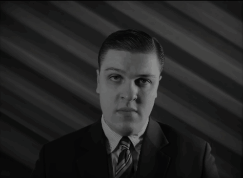 A Man In A Suit And Tie Stands In Front Of The Word Eh. GIF