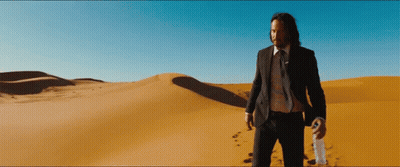A Man In A Suit And Tie Stands In The Desert Holding A Bottle GIF