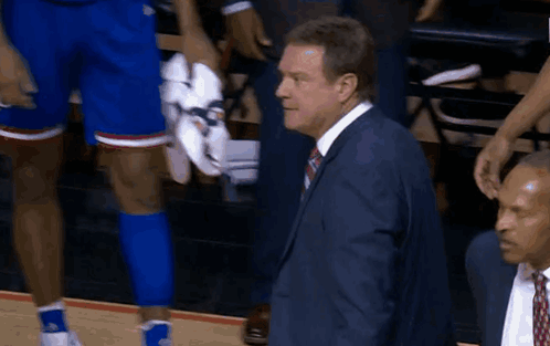 A Man In A Suit And Tie Stands Next To A Basketball Player Holding His Shoes GIF
