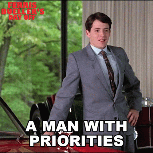 A Man In A Suit And Tie Stands Next To A Red Car With The Words " A Man With Priorities " On The Bottom GIF