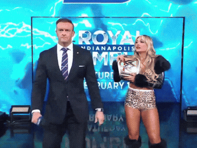 A Man In A Suit And Tie Stands Next To A Woman Holding A Trophy In Front Of A Sign That Says Royal GIF