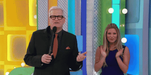 A Man In A Suit And Tie Stands Next To A Woman In A Blue Dress Who Is Clapping GIF