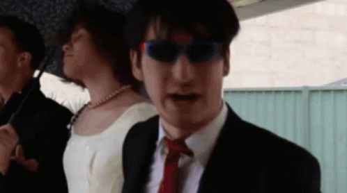 A Man In A Suit And Tie Stands Next To A Woman In A Dress GIF