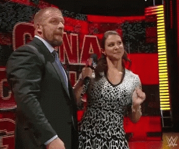 A Man In A Suit And Tie Stands Next To A Woman In A Leopard Print Dress Holding A Microphone .. GIF