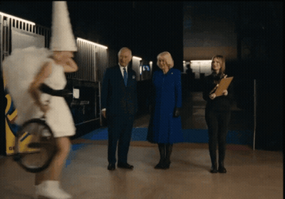 A Man In A Suit And Tie Stands Next To A Woman In A White Dress And A Woman In A Blue Coat GIF