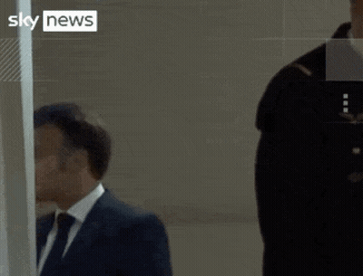 A Man In A Suit And Tie Stands Next To A Woman In A Yellow Vest That Says Sky News GIF