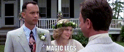 A Man In A Suit And Tie Stands Next To A Woman With A Flower Crown On Her Head And Says Magic Legs . GIF