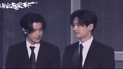 A Man In A Suit And Tie Stands Next To Another Man GIF